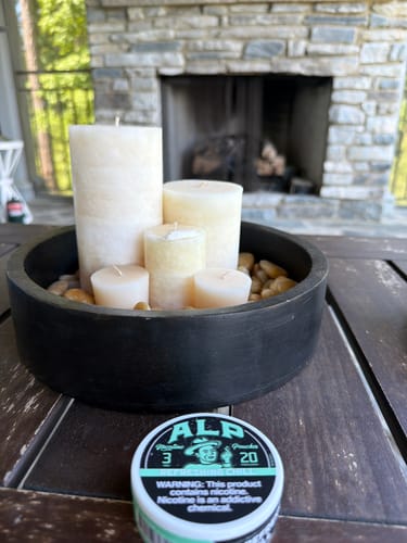 Customer's can of ALP Refreshing Chill Nicotine Pouches on a wooden table in front of a fireplace.