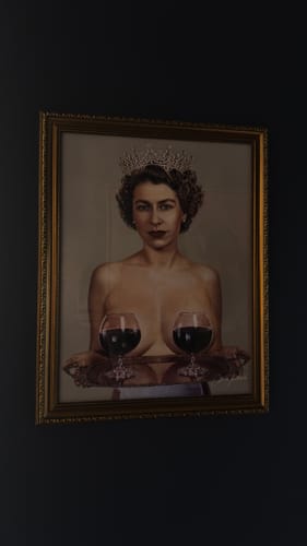 Customer's 'Majestic' art print in an ornate gold frame, showing a woman with a crown and wine glasses, hanging on a dark wall.