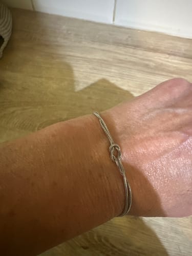 Customer showing a delicate silver knot bracelet worn on their wrist, resting on a wooden surface.