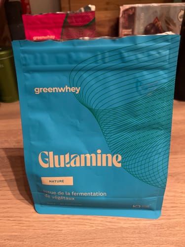 Client montrant le sachet bleu de L-Glutamine greenwhey sur une table en bois.