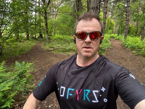Reviewer in the black Invasion jersey with a colorful logo, standing on a wooded trail.
