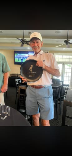 Reviewer, a smiling man, holding up a round, dark prize plate from a golf club.