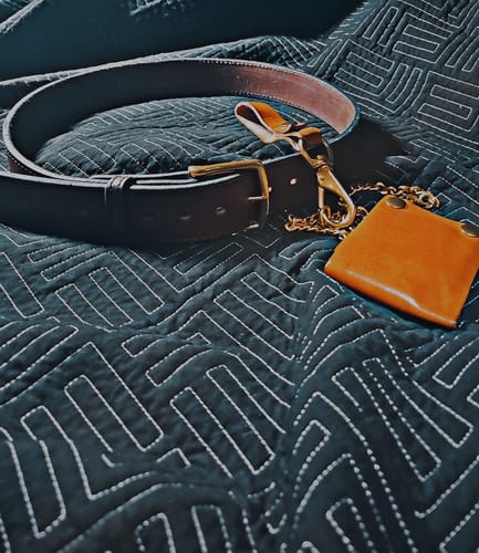 Customer's dark leather Xtreme 1.75" belt with a brass buckle, coiled on a dark patterned quilt.