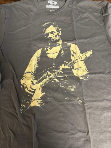 Customer's grey Lincoln Guitar T-Shirt with a gold graphic of Abraham Lincoln playing an electric guitar.