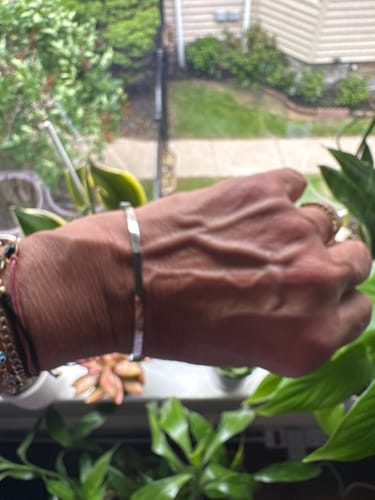 Close-up of a reviewer's wrist wearing the delicate 14K White Love Bangle Bracelet indoors.
