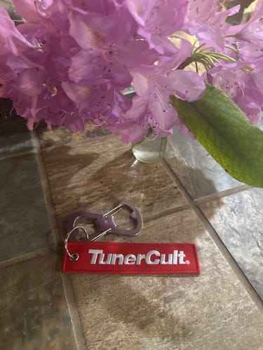 Customer's red TunerCult jet tag keychain with a metal ring, resting on a tiled surface next to flowers.