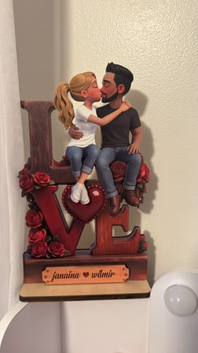 Customer's personalized wooden plaque with a figurine of a couple kissing on top of the word LOVE, adorned with red roses.