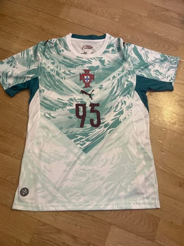 Photo d'un client montrant le maillot du Portugal à motif blanc et vert avec le numéro 95, posé sur un sol en bois.