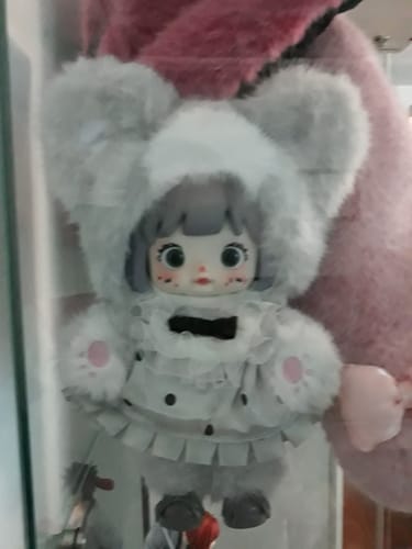 Close-up of a reviewer's Nommi Forest Kingdom 'Curly-Tail Kitty' figure, wearing a fuzzy grey cat hood and a cute polka-dot dress.
