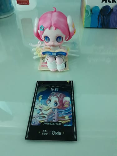 Customer's pink-haired Ossia Feel the World figure sitting and reading a book, with its collector's card in front.