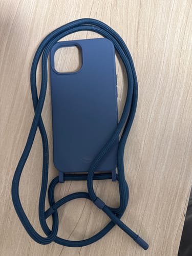 Cliente mostrando a Cordinha Odara Azul da Cor do Mar em uma capa de celular sobre uma mesa.
