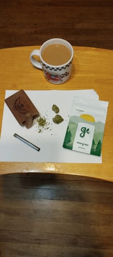 Customer's Blue Dream flower and ground cannabis on a table with a one-hitter pipe, packaging, and a coffee mug.