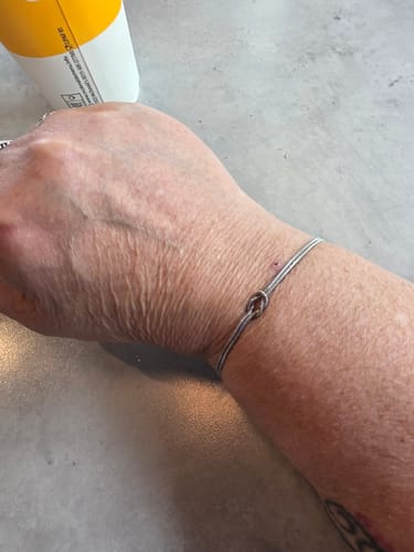 Customer's wrist wearing a delicate silver-colored bracelet with a simple knot design.