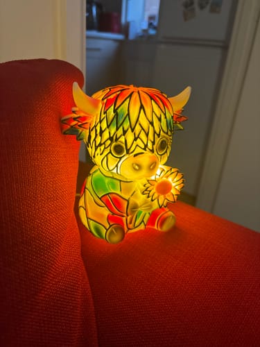 Customer's multicolored Highland Cow LED Night Light glowing warmly on a red couch.
