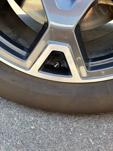 Close-up of a customer's dark 80Eighty Valve Stem Cap installed on a silver car wheel.