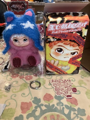 Customer unboxing a KikaGoods Handmade Keychain, showing a pink plush figure in its packaging and box.