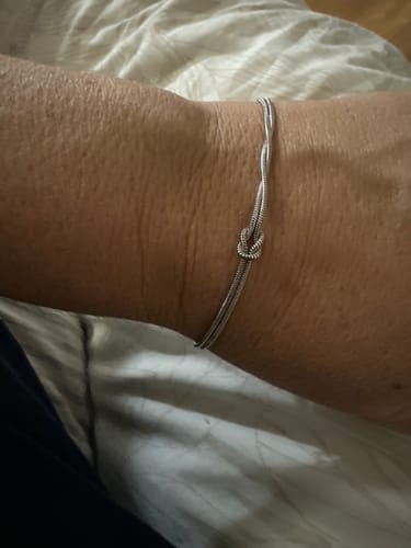Customer showing a delicate silver-colored knot bracelet on their wrist.