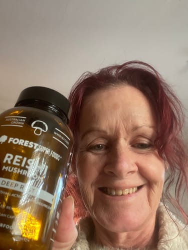 Reviewer smiling while holding a bottle of Australian Grown Reishi Mushroom Capsules.