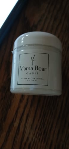 A customer's white jar of Mama Bear Nerve Relief Lotion resting on a dark wood surface.