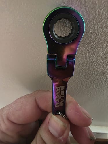 Reviewer holding the iridescent 10mm Wrench Keychain, showing the engraved text 'In Speed We Trust'.