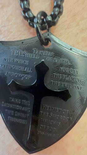Close-up: Customer's black shield pendant showing engraved text and a cross cutout.