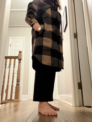 Customer's side view of a long, plaid shirt-jacket mystery item worn over black pants in a hallway.