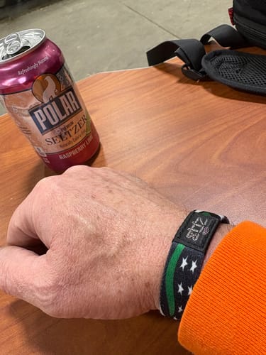 Close-up of a reviewer wearing the Hold the Line Hero Bracelet, showing its black fabric and green line flag design.