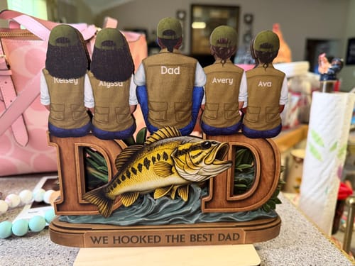Customer's personalized wooden plaque with a dad and four kids in fishing vests, sitting on the word 'DAD' with a large fish.