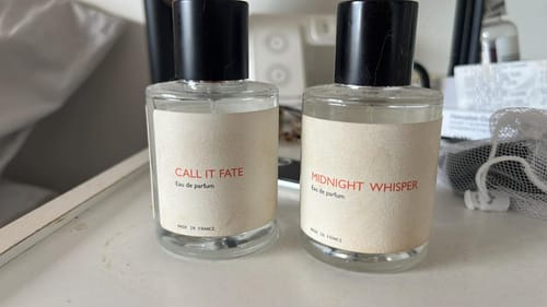 Reviewer's 'Call It Fate' and 'Midnight Whisper' perfume bottles sitting side-by-side on a white surface.