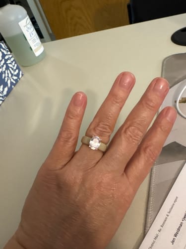 Customer's hand wearing the Silicone Ring with a large oval-cut stone and a light-colored band, shown on an office desk.