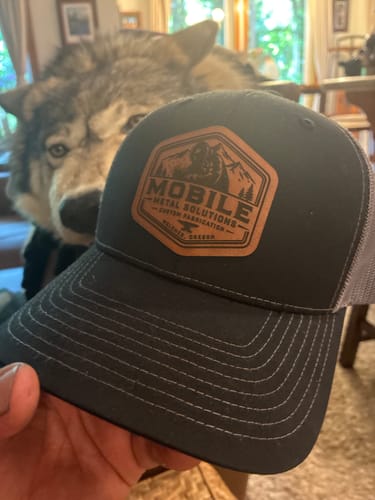 Customer holding a black Custom Leather Patch Trucker Hat with a custom logo on the brown leather patch.