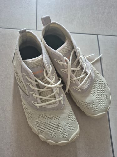 Foto eines Kunden, das ein Paar helle, perforierte Schuhe mit weißen Schnürsenkeln auf einem Fliesenboden zeigt.