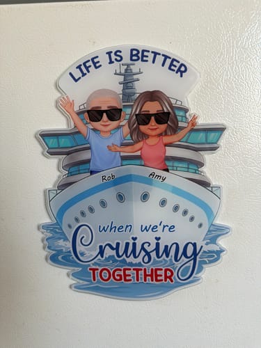 Customer's personalized cruise ship magnet, featuring a cartoon couple and names, shown on a white refrigerator door.
