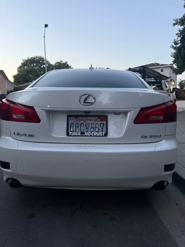 Reviewer's black TUNA NO CRUST LICENSE PLATE FRAME installed on the back of a white car.
