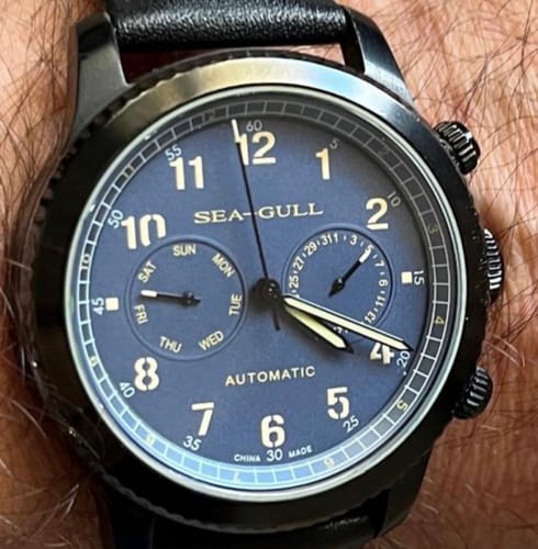 Customer's automatic watch with a detailed blue dial, black case, and day and date subdials, worn on a wrist.