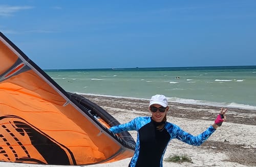 Una clienta en la playa junto a un equipo de kitesurf, mostrando su recuperación tras usar el Protocolo Wolverine Stack.