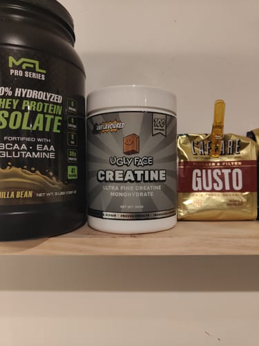 Customer's white tub of UGLYFACE CREATINE MONOHYDRATE sitting on a wooden shelf next to other products.