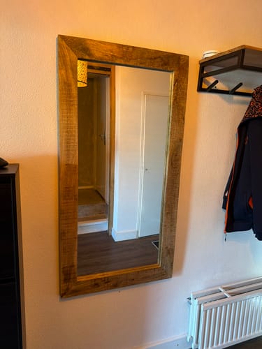 Klantfoto van de industriële mangohouten spiegel, verticaal opgehangen aan een muur in een hal.