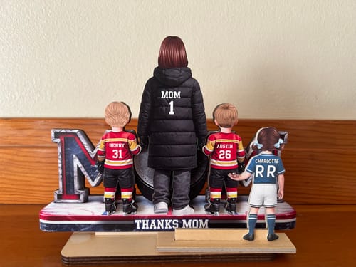 Customer's personalized hockey mom plaque with two boys, shown with a reviewer-added daughter figure on a wooden stand.