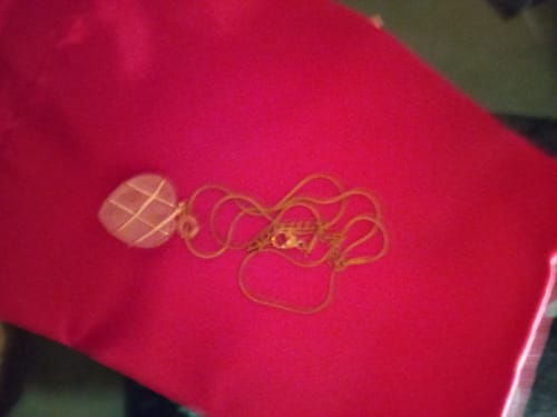 Reviewer's wire-wrapped Rose Quartz necklace with a heart-shaped pendant and gold chain, displayed on a red cloth.