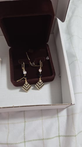 A customer's Sujata Earrings with a sparkling diamond-shaped design, displayed in their original brown jewelry box.