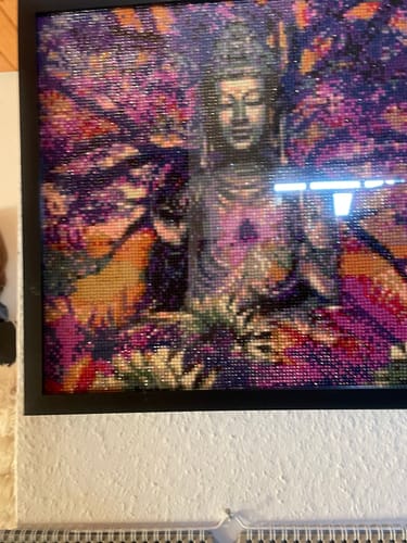 Kunde zeigt das fertige Diamond Painting „Buddha-Baum violett orange“ in einem schwarzen Rahmen an einer Wand.