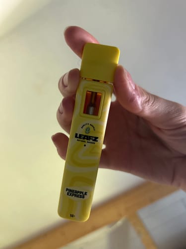 Ein Kunde hält den gelben Live Resin PHC Vape mit der Aufschrift „Pineapple Express“ in der Hand.
