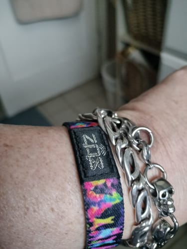 Close-up of a reviewer wearing their colorful Love Stays Bracelet next to a silver link bracelet on their wrist.