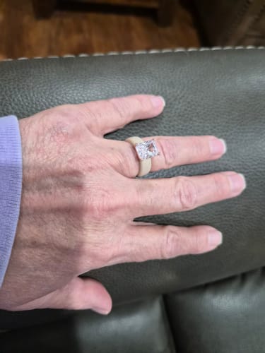 A reviewer's hand wearing the Silicone Ring, showing the large emerald-cut CZ stone on the light-colored band.