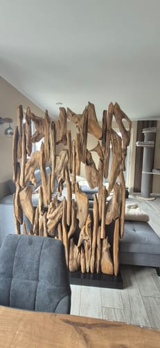Kunde zeigt den BELMIRO Holz-Raumteiler aus massivem Teakholz, der in einem Wohnzimmer als Trennwand aufgestellt ist.