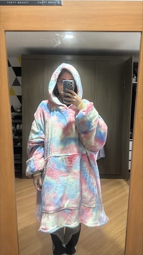 Cliente tirando uma selfie no espelho com seu cobertor vestível Sleepo Tie Dye. A peça grande e colorida tem capuz.