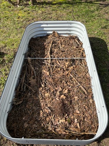 Close-up of a customer's 17” Tall Modular garden bed being filled with leaves and sticks in a backyard.