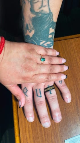 A customer shows their black tungsten Huntress ring on their tattooed hand, next to a partner's hand.