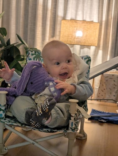 Customer's baby sits happily in the patterned Sailor baby chair v2 on a wooden table.